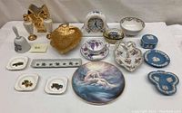 Photo showing the entire set of 17 porcelain and ceramic collectibles including clock, trinket boxes, small plates, decorative plate, bells, leaf-shaped tray, and other items.