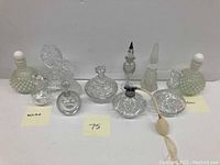 Full lot of 10 vintage glass perfume bottles arranged in two rows on a white surface, showing variety in shapes and stopper styles. Two sticky notes label Waterford and Fenton bottles.