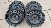 Four black steel winter rims arranged on ground, showing circular holes and surface rust