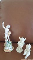 Three cherub figurines displayed together on a brown surface, showing styles and sizes.
