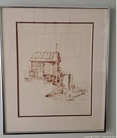 Framed etching showing rustic wood cabin on dock with various dock items, matted and framed in silver frame