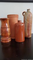 Photo showing four vases including a wooden vase, terracotta wine cooler, brown glazed ceramic vase, and tall grey brown jug with handle.