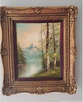 Full view of the framed landscape oil painting showing trees, lake, mountains, and sky.