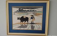 Framed artwork showing a person leading a water buffalo in a stylized rice field, mounted with blue mat and simple frame.