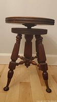 Full side view of the vintage adjustable piano stool showing the turned legs, carved supports and claw feet.