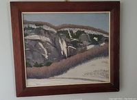 Framed landscape oil painting depicting rocky cliffs and natural scenery, signed by artist in lower right.