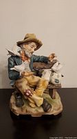 Front view of ceramic figurine showing tramp with birds on his hands and shoulders, seated on bench.