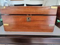 Closed view of rectangular Victorian wooden box with brass corner protectors and keyhole