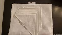Folded white polyester tablecloth with six matching napkins on top, showing full set and texture