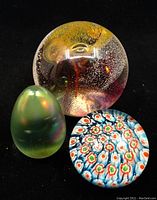 Image showing all three glass paperweights together: green egg-shaped, millefiori floral pattern, and abstract round paperweight with bubbles.