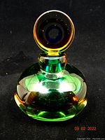 Front view of hand crafted art glass perfume bottle in green and amber with round stopper.