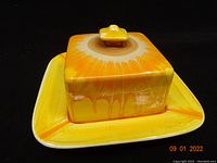 Butter dish with lid on base plate showing bright yellow and orange drip glaze decoration.