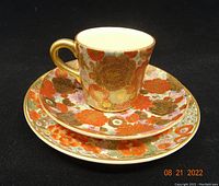 Tea cup posed on saucer and snack plate showing intricate floral and butterfly hand painted designs with gold detailing