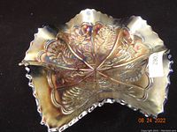 Full view of the iridescent carnival glass bowl with scalloped edge, showing the embossed peacock and dahlia panels.