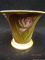 Side view of the tapered chocolate cup showing hand painted purple/white tulip and green leaves on mustard yellow glaze with gold trim near the base