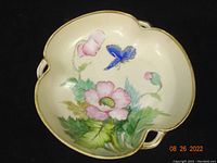 Top view of Nippon hand-painted dish showing butterfly, pink flower, and gilt edged scalloped rim with handles.