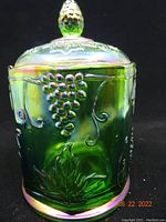 Front side view of the green carnival glass canister showing embossed grape clusters and leaves with iridescent finish.