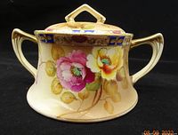 Front and side view of the biscuit jar showing overall shape, dual handles, floral decoration and gilt accents.