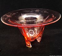 Pink depression glass vase with wide flared rim, etched floral pattern, and three-legged base resembling a rocket shape.