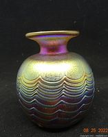 Front and side view showing the round body with scalloped wave pattern and iridescent surface.