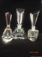 Front view showing all three clear crystal perfume bottles with geometric faceted stoppers and bases on black background.