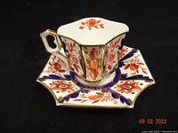 Full view of Wileman Imari quatrefoil style teacup placed on matching saucer showing overall hand-painted floral and gilt design.