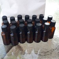 Twenty amber glass bottles arranged in rows showing black caps and amber glass bodies.