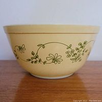 Side view of a yellow Pyrex bowl with green floral vine pattern on exterior