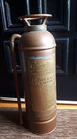 Full front angled view of the copper and brass antique fire extinguisher showing body and top handle.