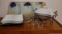 Glass serving dishes, ceramic chafing dish on metal stand, and floral divided serving tray on a wooden surface