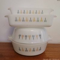 Four Fireking Candle Glow white opaque glass bakeware pieces stacked on wooden surface, showing pattern and condition.