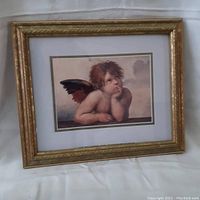 Framed print of a cherub with hand under chin, approximate size 10x12 inches, gold-tone wood frame with glass front