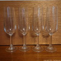 Four clear tall champagne flutes shown upright against a wood background with no visible damage or wear.