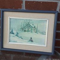 Framed print showing winter cabin scene with children sitting in the snow, signed by Keirstead.