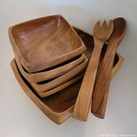 Four square wooden salad bowls stacked and a pair of wooden salad serving utensils laying on top.