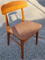 Front side view showing the full chair with brown upholstered seat and wooden back, casting shadow on concrete floor.