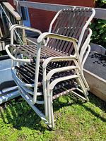 Four stackable retro metal patio chairs with slatted seats and backs, cream-colored frames, and brown slats, placed outdoors on grass near a railing.