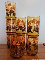Set of 8 vintage amber juice glasses stacked, showing autumn maple leaf print in orange and brown.