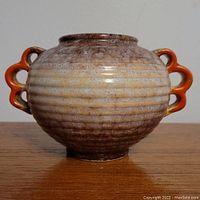 Front view of round pottery vase showing ribbed texture and two orange double-loop handles