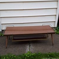 Front view of the vintage coffee table showing the laminate surface, metal side rails, and wooden tapered legs on outdoor concrete ground.