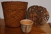 Photo showing woven planter basket, small pottery planter, and wooden sunflower trivet on wooden surface