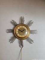 Full front photo of vintage starburst clock showing the radiating metal rod design and round dial with Roman numerals.