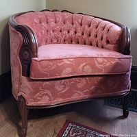 Front angled view showing the curved shape, tufted pink upholstery and carved wood on arms and legs.