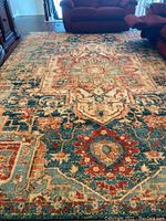 Full view of the large area rug displaying cream, turquoise, and rust colors with traditional patterns, set in a living room environment