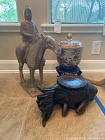 Photo showing the mounted horseman statue, ceramic ginger jar on wooden stand, and wooden fish stool to present the lot contents.