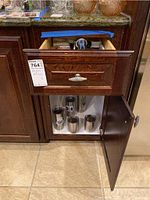 Open kitchen drawer showing barware items inside and cabinet below containing four Yeti cups and metal thermos.