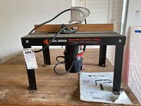 Full view of Black & Decker router/jigsaw table showing router mounted underneath table surface with owner's manual alongside.