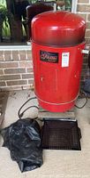 Full view of red Brinkman Gourmet electric smoker with power cord and black cover on floor beside it, showing overall condition and size.