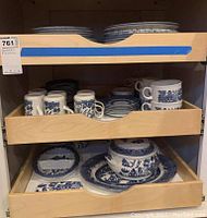 Three pull-out drawers showing stacks of plates on top, mugs and saucers in middle, assorted serveware below
