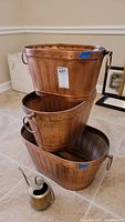 Three stacked copper-tone metal pails with watering can at front